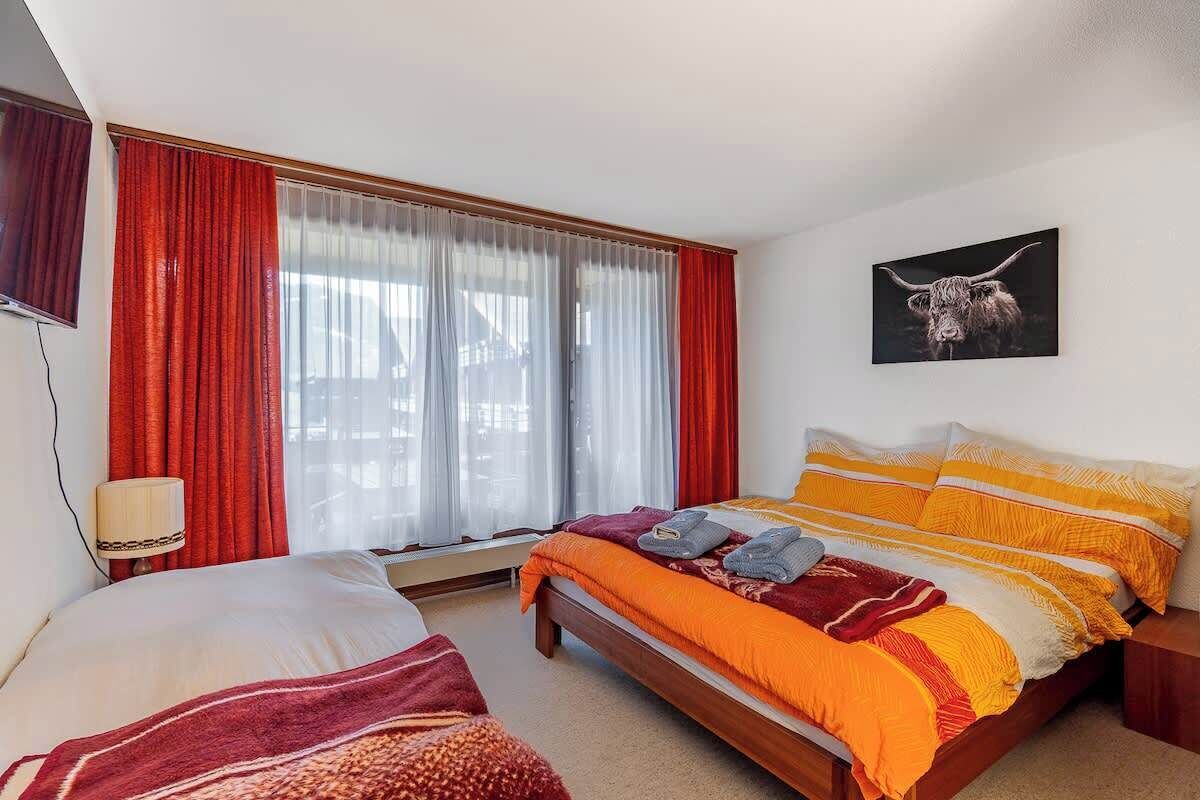 A hotel room with a bed, a bedside table, a lamp, and a window with curtains.