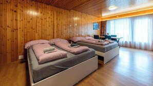 Une chambre avec deux lits, des murs en bois, un bureau et une fenêtre avec des rideaux.