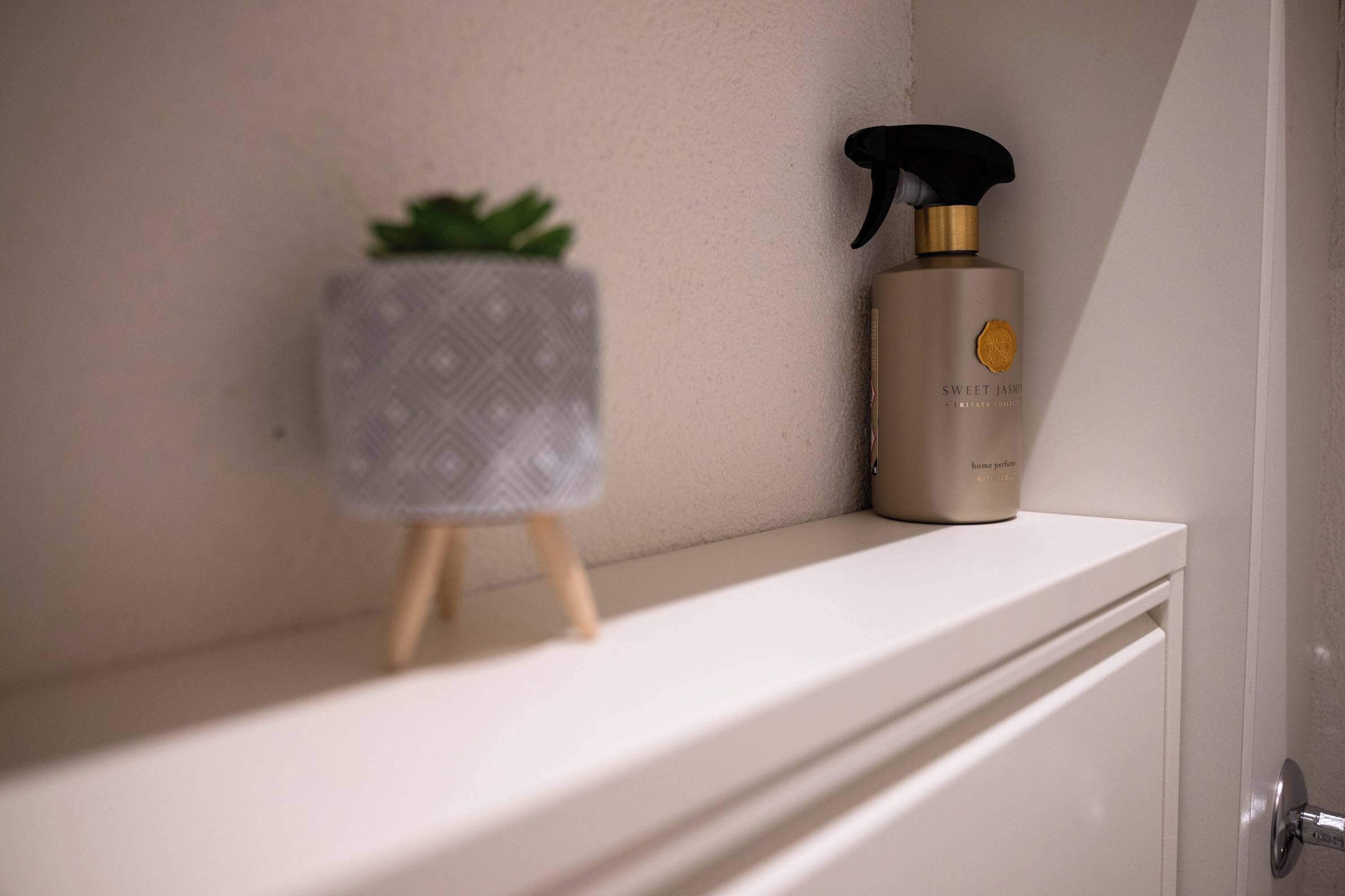 Uma prateleira no banheiro com uma pequena planta em vaso e um frasco de loção corporal Sweet Jasmine.