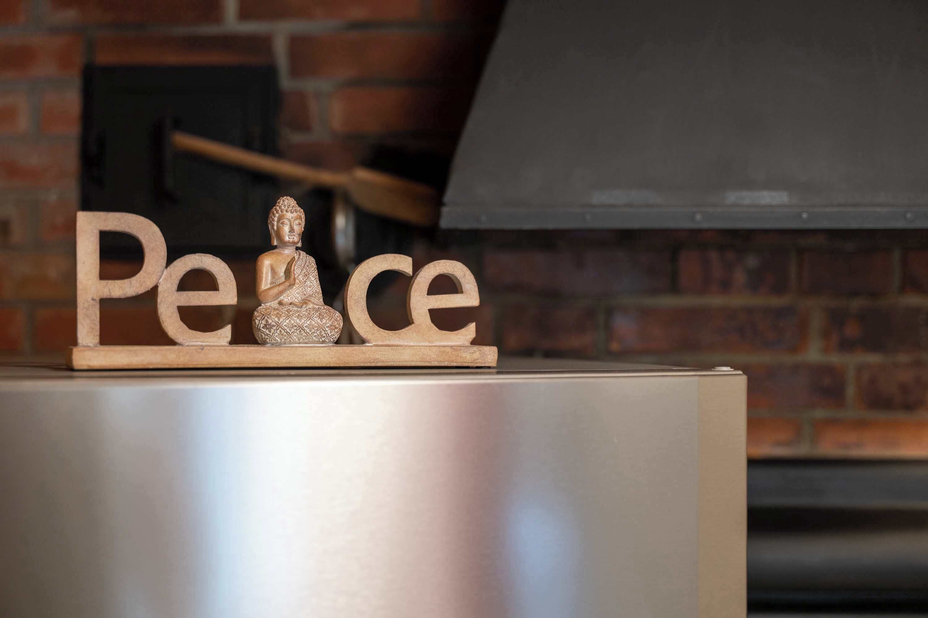 Eine Buddha-Statue und hölzerne Buchstaben, die das Wort "Peace" auf einer Metallfläche bilden.