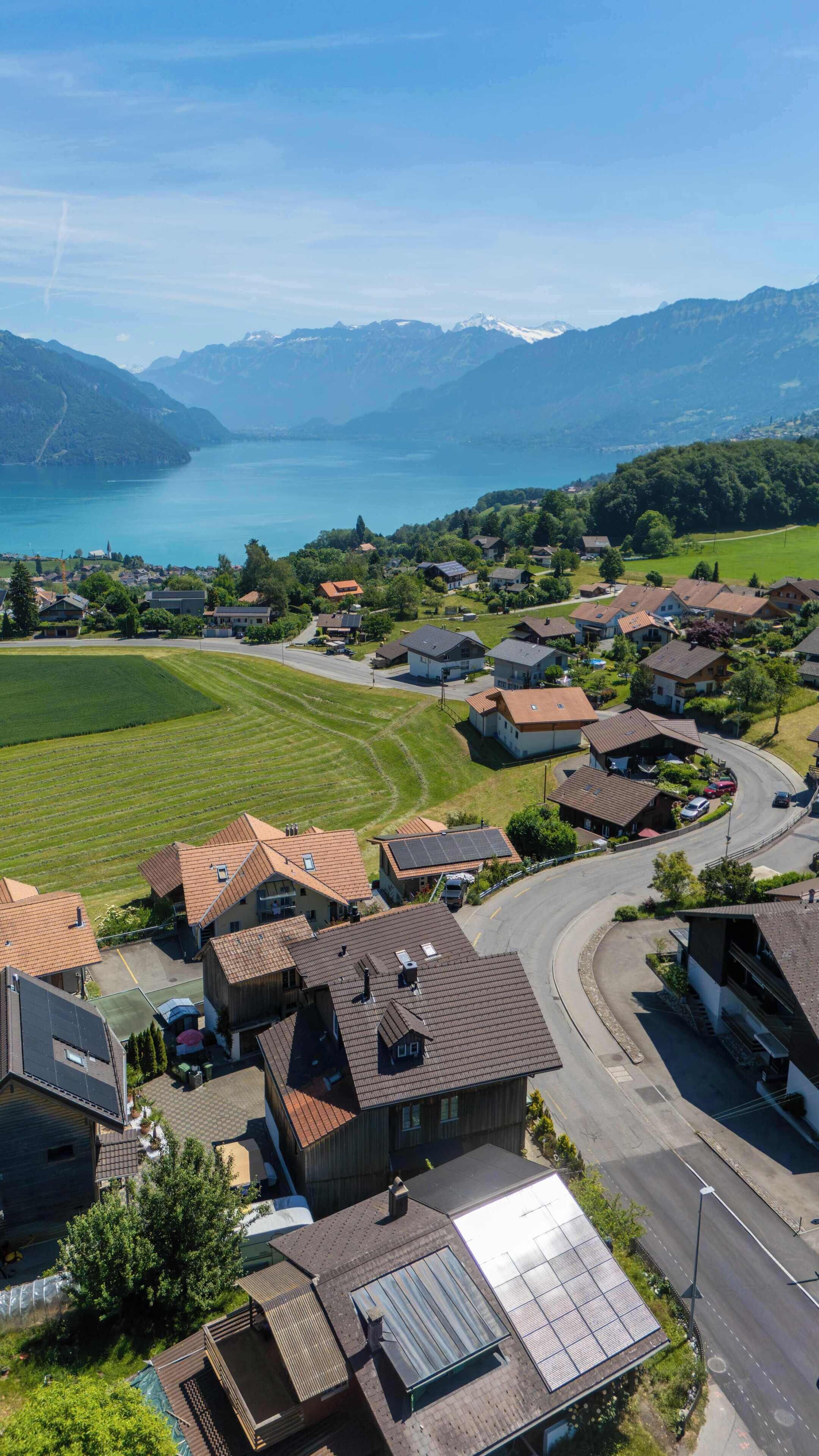 Ein Wohngebiet mit Häusern, einer Straße und einem See mit Bergen im Hintergrund.