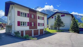 A modern two-story building with a white facade and red shutters, set against a mountainous backdrop.