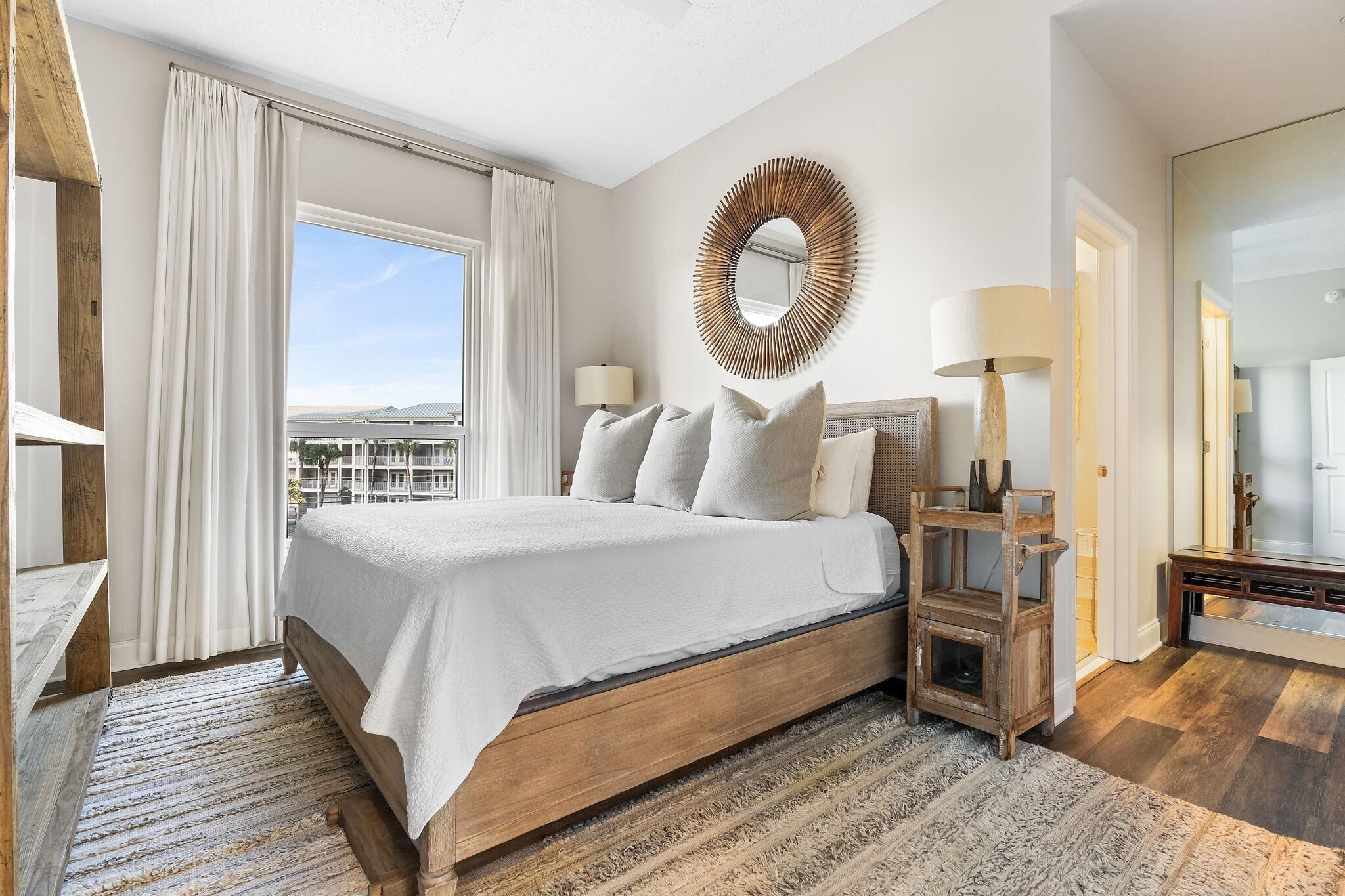 Een moderne hotelkamer met een groot bed, een ronde spiegel en uitzicht op de stad.