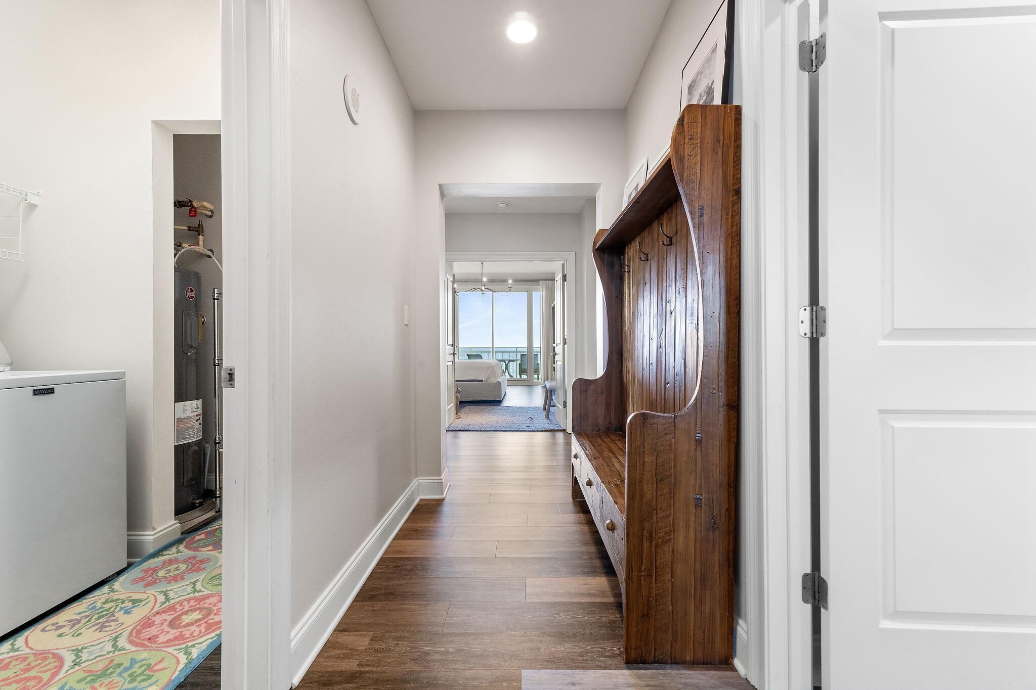 A hallway with a wooden bench, a white door, and a refrigerator.