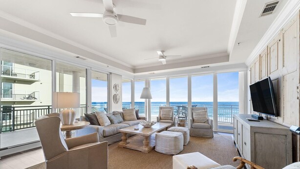 Uma sala de estar ampla com uma grande janela com vista para o oceano, mobiliada com um sofá, cadeiras e uma mesa de centro.