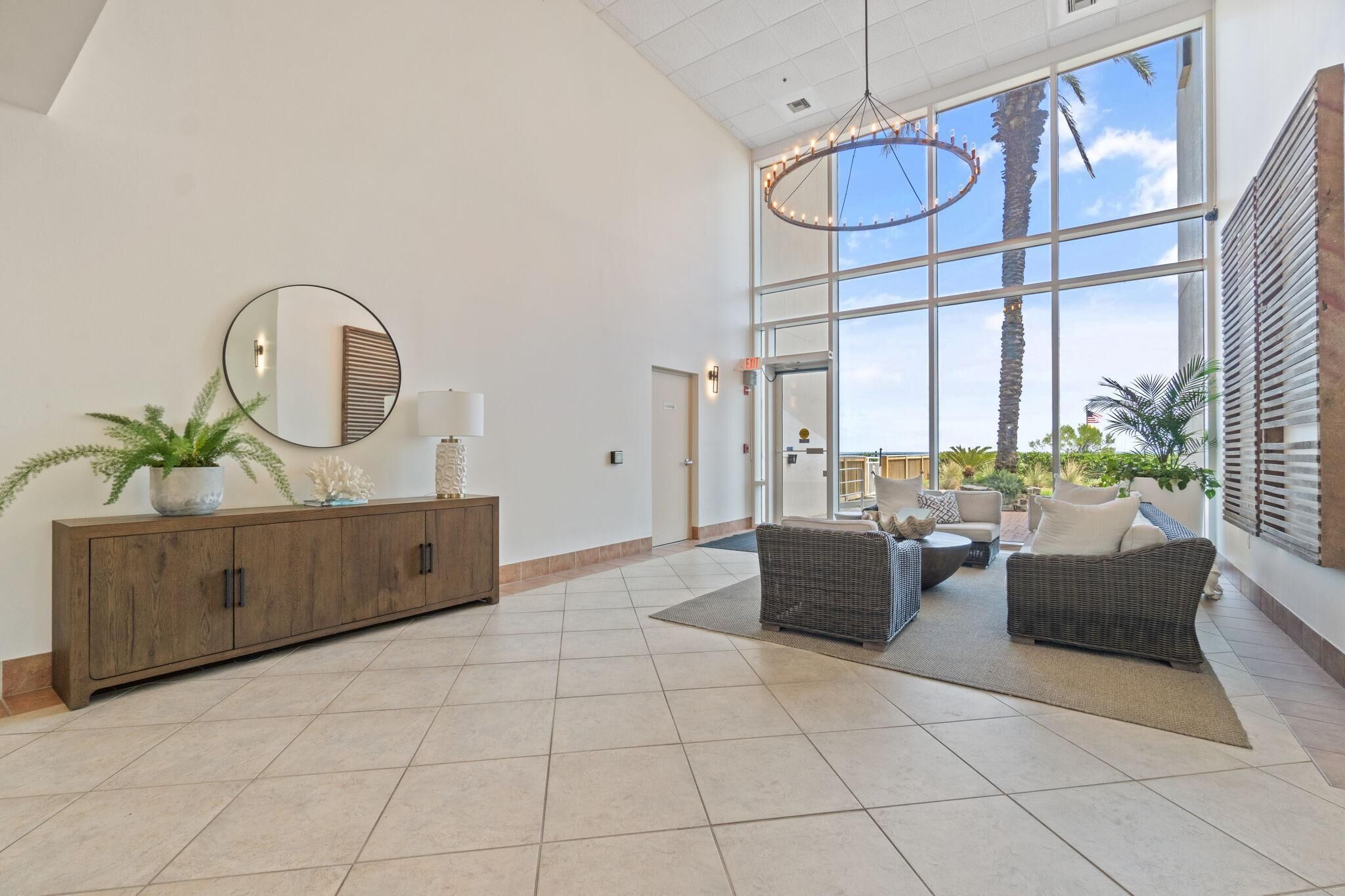 Een ruime lobby met een groot raam, een houten console tafel met decoratieve objecten, en een zithoek met rieten meubels.