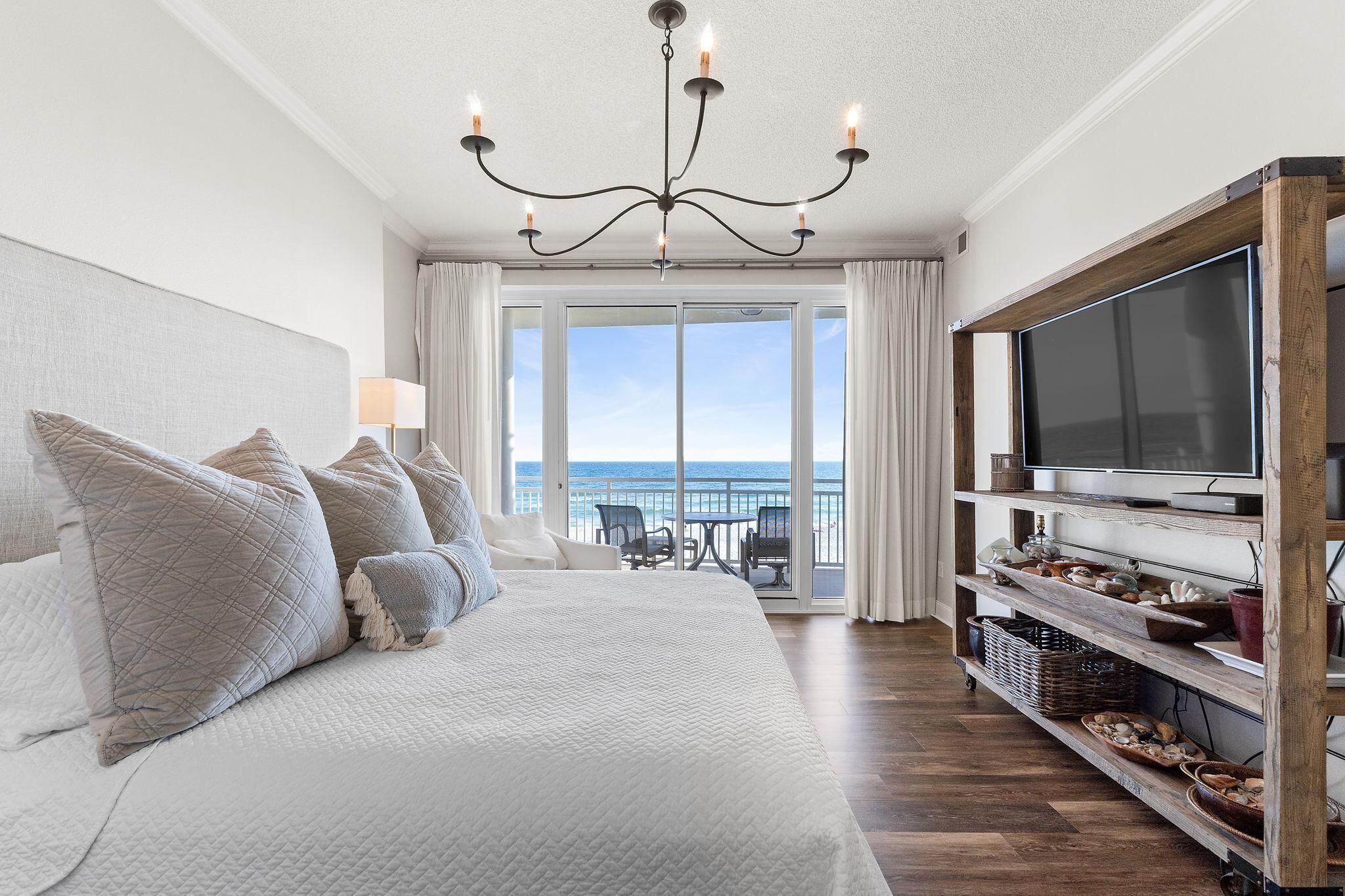 A bedroom with a large bed, a TV, and a view of the ocean.