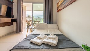 A hotel room with a bed, a TV, a balcony with a view, and a painting on the wall. - 200m da praia c piscina e churrasqueira (Bertioga)