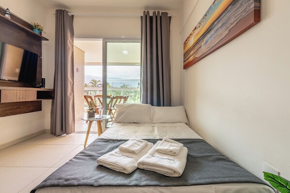 A hotel room with a bed, a TV, a balcony with a view, and a painting on the wall. - 200m da praia c piscina e churrasqueira (Bertioga)
