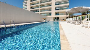 A swimming pool with clear blue water, surrounded by a white tiled deck and lounge chairs. - 200m da praia c piscina e churrasqueira (Bertioga)