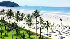 A beach with palm trees, umbrellas, and a clear view of the ocean. - 200m da praia c piscina e churrasqueira (Bertioga)