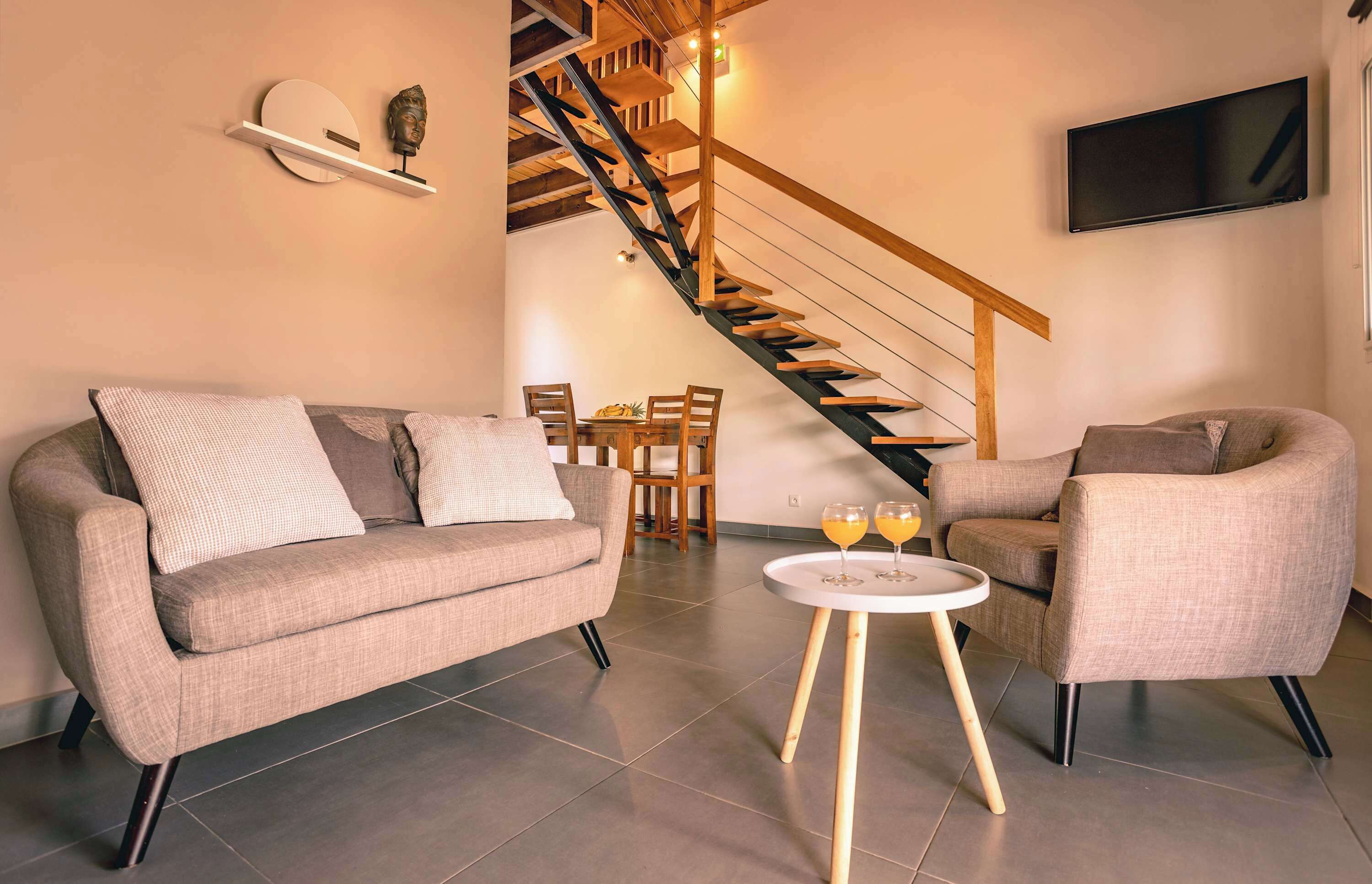 Een woonkamer met een bank, fauteuil, salontafel en een trap.