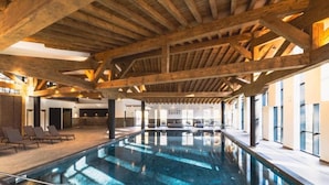 An indoor swimming pool with wooden beams, lounge chairs, and large windows. - Apartment with Mont Blanc View & Spa (MEGEVE)