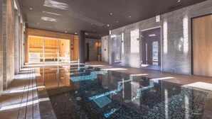 A modern hotel lobby with a reflective floor, a wooden seating area, and a large glass door. - Apartment with Mont Blanc View & Spa (MEGEVE)