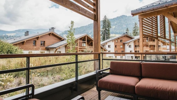 A wooden deck with a sofa and a view of mountain houses. - Apartment with Mont Blanc View & Spa (MEGEVE)