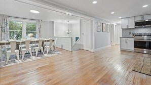 A spacious kitchen with white cabinetry, a stainless steel oven, and a dining area with a wooden table and chairs. - Dual Home Retreat! Walk Between Both! Sleeps 28! Dogs OK! (Newfield)