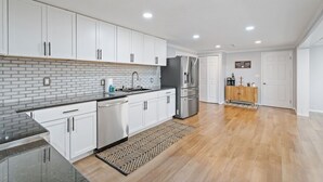 A modern kitchen with white cabinets, a brick backsplash, stainless steel appliances, and a wooden floor. - Dual Home Retreat! Walk Between Both! Sleeps 28! Dogs OK! (Newfield)