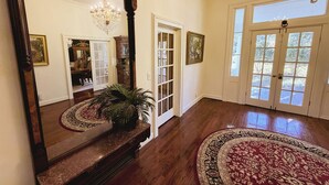 Un vestíbulo amplio con un espejo grande, piso de madera, un candelabro y un ventanal.