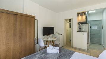 A hotel room with a bed, a TV, a small dining table with chairs, a kitchenette, and a wardrobe.