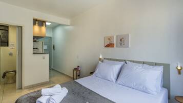 A hotel room with a bed, a bedside table, a nightstand, a wall-mounted light, and a door leading to a bathroom.
