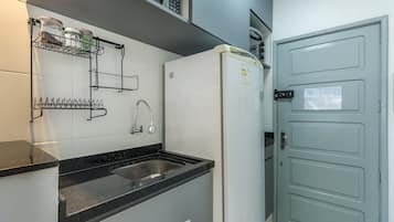 A compact kitchen with a sink, a refrigerator, and a door with a notice.