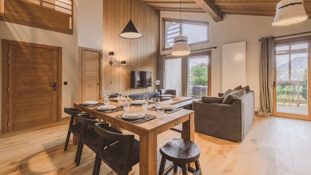 A modern interior with a wooden dining table set for four, a sofa, and a TV mounted on the wall. - Spacious Alpine Apartment with Jacuzzi (MEGEVE)