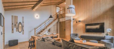 Un salon moderne avec un plafond en bois, un escalier, un téléviseur à écran plat et un coin repas.