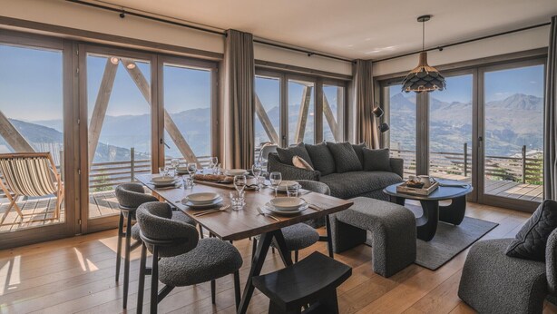A modern dining area with a wooden table set for four, large windows with mountain views, and a cozy seating area with a sofa and armchairs. - Family Retreat in Peisey-Vallandry (Plan Perisey)