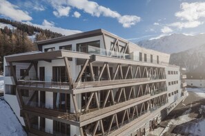 En modern byggnad med en glasfasad, flera balkonger och en bergig bakgrund.