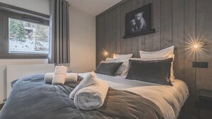 A bedroom with a large bed, dark wood paneling, a window with curtains, and a wall-mounted picture. - Apartment in Peisey-Vallandry for 10 (Plan Perisey)