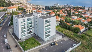 A modern building with multiple floors, a parking lot, and a view of the sea and a hillside town. - Studio Palace B by Homie (Funchal)