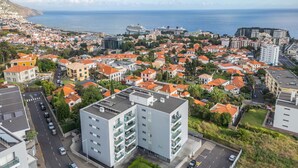 A modern building with multiple floors, a parking area, and a view of the sea and cityscape. - Studio Palace B by Homie (Funchal)