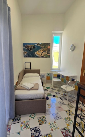 Une chambre à coucher comprenant un lit, une fenêtre, une chaise, une table et un tableau représentant un paysage côtier.