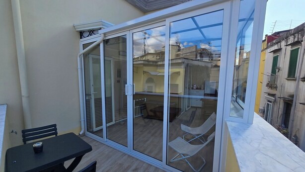 Uma varanda com porta de vidro, uma mesa com uma cadeira e vista para prédios vizinhos.