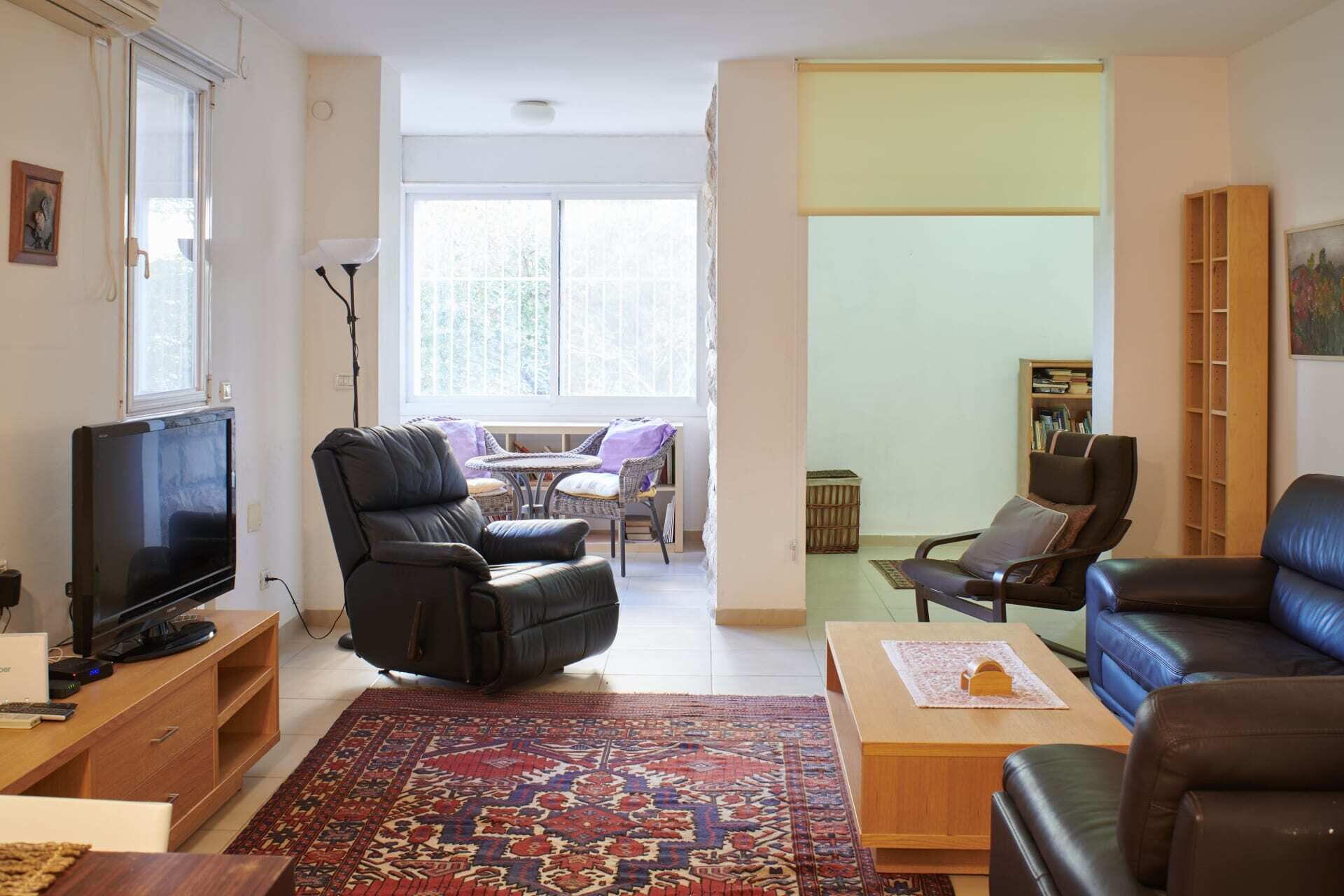 Una sala de estar con televisor, sillones de cuero, alfombra estampada y una estantería.
