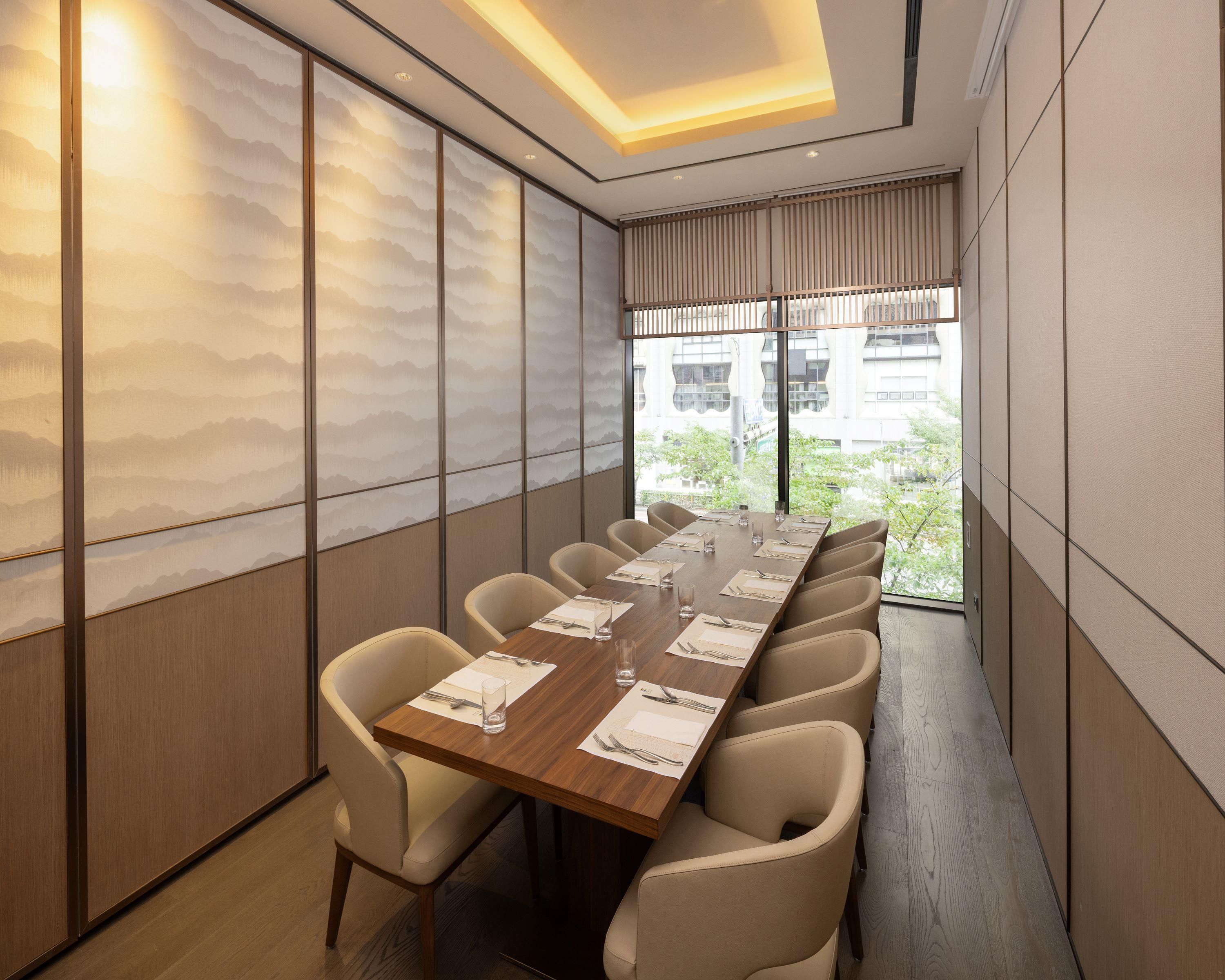 A conference room with a long table, multiple chairs, and a view of the outdoors through large windows.