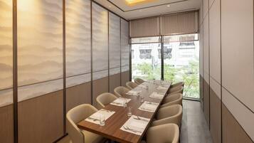 A conference room with a long table, multiple chairs, and a view of the outdoors through large windows.
