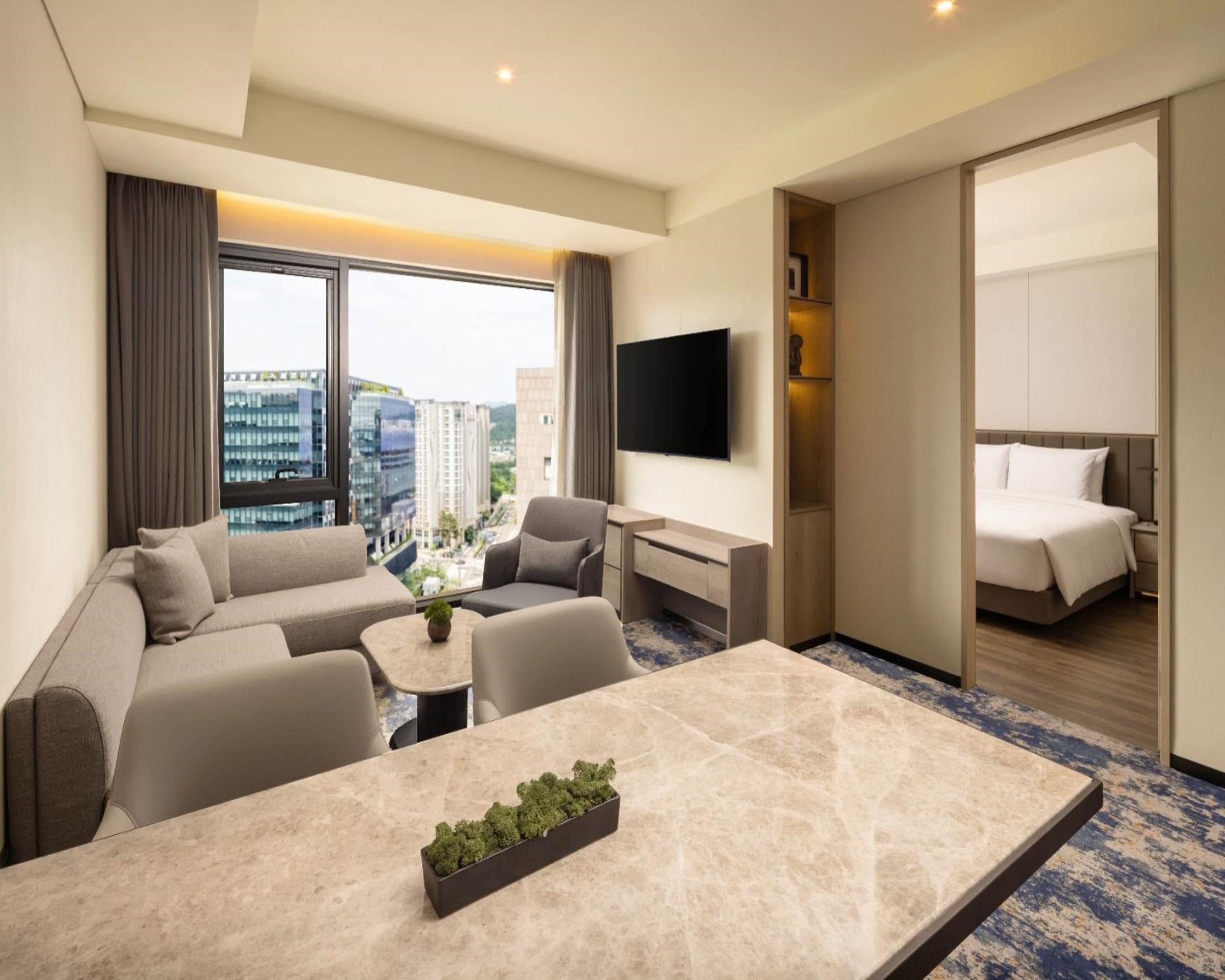Ein Hotelzimmer mit einer Couch, Sesseln, einem Esstisch, einem Fernseher und einem Bett.
