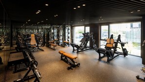 Un gimnasio con diverso equipo de ejercicio, bancos y amplias ventanas que dejan entrar luz natural.