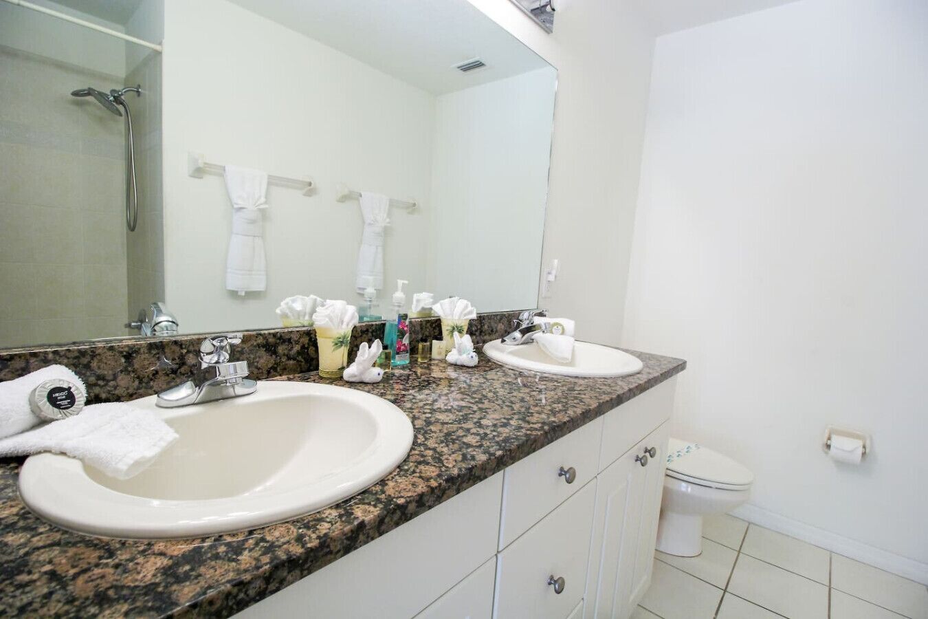 A bathroom with two sinks, a shower, and a toilet. There are towels and toiletries on the counter.