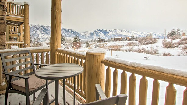 A wooden balcony with a table and chairs, overlooking a snowy landscape with mountains in the background. - Eden Poolside Condo! Hottub + 3 nearby ski resorts (Eden)
