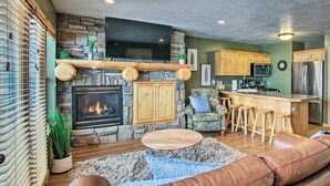 A cozy living room with a stone fireplace, a flat-screen TV, a comfortable leather sofa, and a bar area with stools. - Eden Poolside Condo! Hottub + 3 nearby ski resorts (Eden)