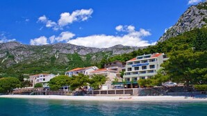 Un hotel sulla costa con diversi edifici, una spiaggia e montagne sullo sfondo.