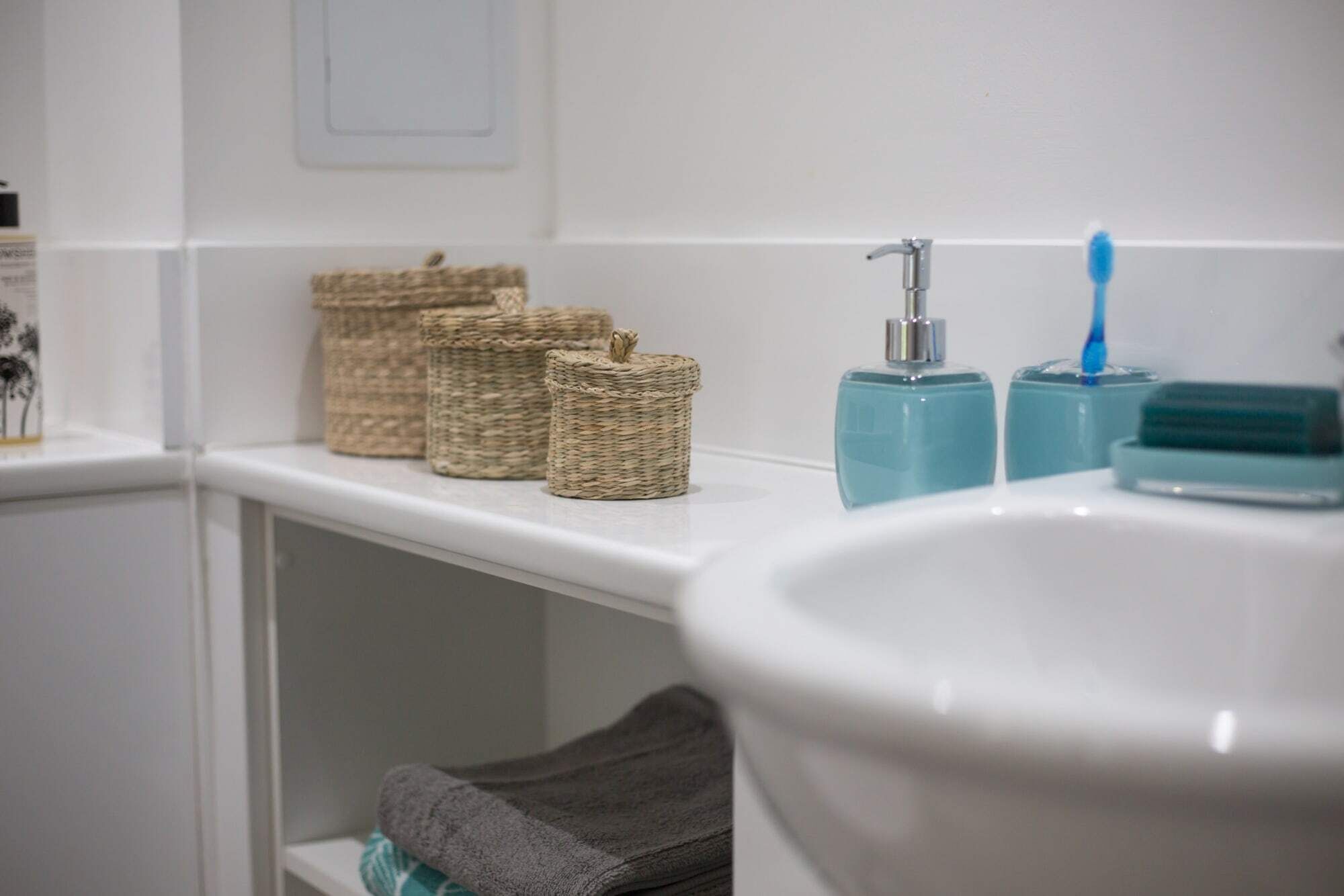 A bathroom with a white sink, two toothbrush holders, and three wicker baskets on the shelf.