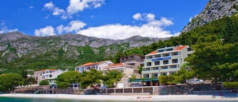 A coastal hotel with multiple buildings, a beach, and mountains in the background.