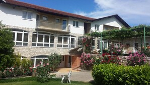 Ein zweistöckiges Haus mit einer Steinaußenfassade, einem Balkon und einem Garten mit rosa Blüten.