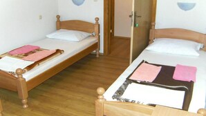 Dos camas individuales con cabeceros de madera y ropa de cama blanca, suelo de madera y una puerta que da a otra habitación.