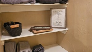 Un baño con repisas que sostienen toallas, una cesta y un cartel enmarcado.