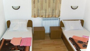 Ein kleiner, sauberer Raum mit zwei Einzelbetten, Holznachtischen, einem Heizkörper und einem Fenster mit einem gemusterten Vorhang.