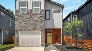 Une maison à deux étages avec un garage, une façade en pierre et un petit jardin devant la maison, avec un arbre.